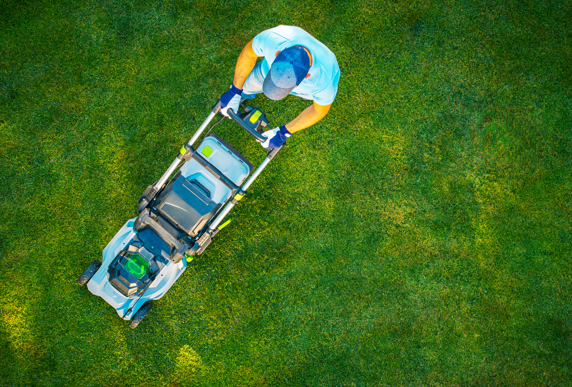 A Person Mows a Lush Green Lawn With a Modern Mower on a Sunny Day in a Residential Area